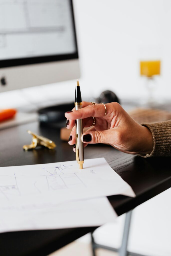A woman's hand holding a pen, working on paperwork in a modern office setting.